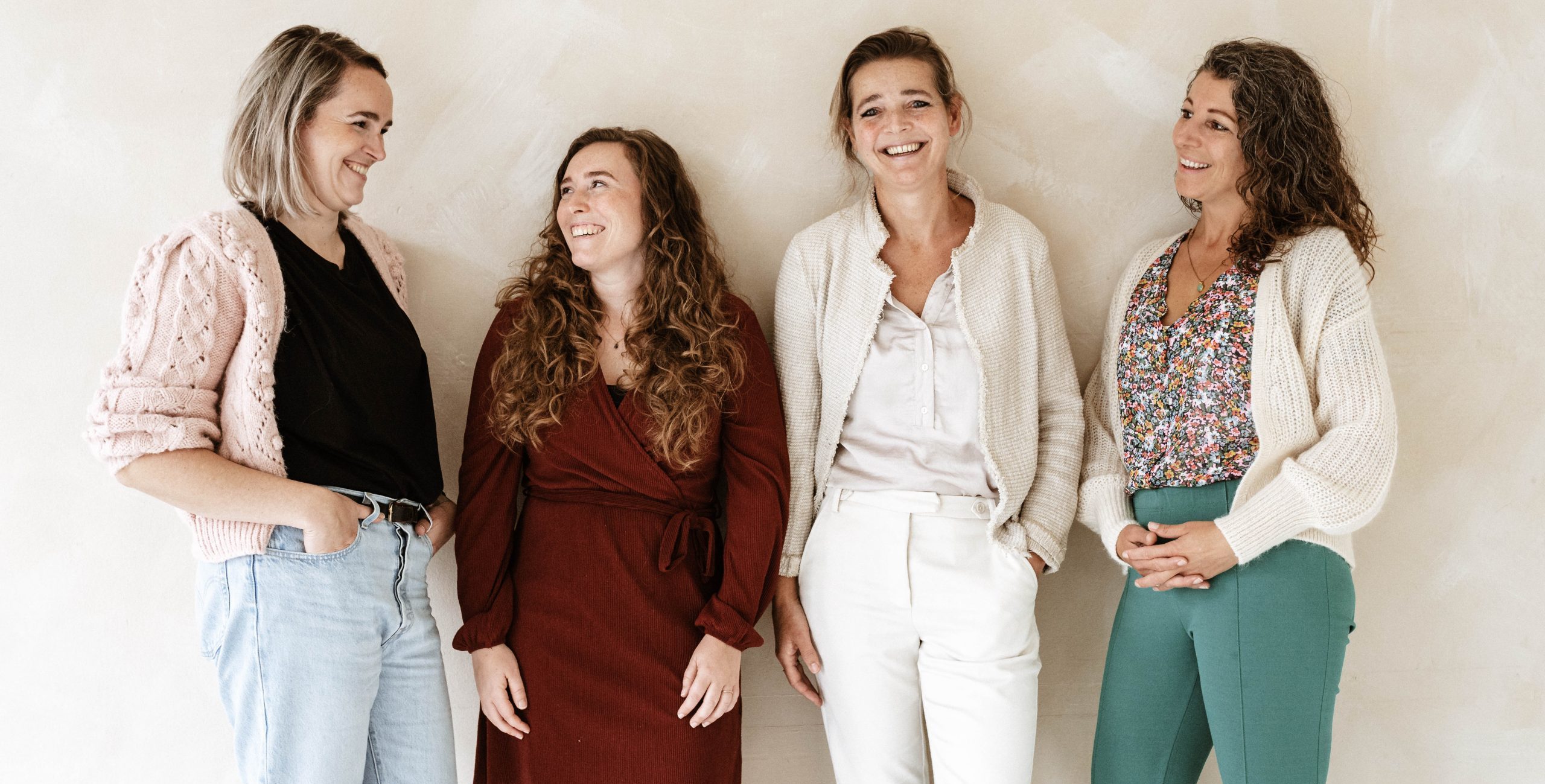 Vier vrouwen staan lachend voor een muur